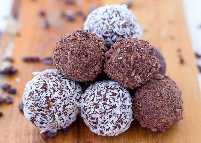 A pile of cacao maca energy bites made with Navitas Organics Cacao Powder and Maca Powder, rolled in shredded coconut and Navitas Organics Cacao Nibs.