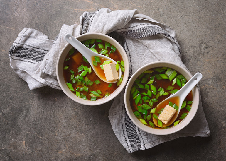 Two bowls of miso soup made with Navitas Organics Superfood+ Sea Veggie Blend, garnished with tofu and green onions.