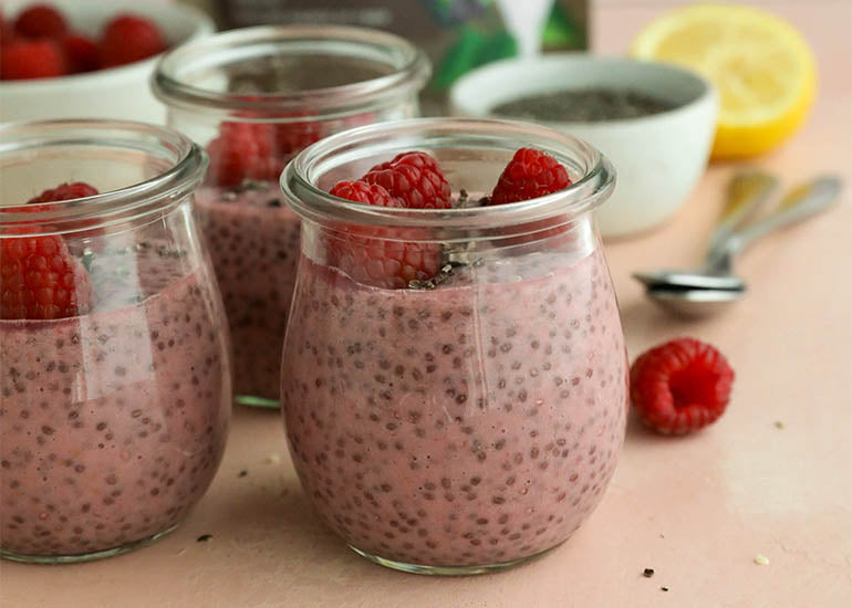 Three glass jars filled with raspberry chia pudding made with Navitas Organics Chia Seeds, topped with fresh raspberries and Navitas Organics Hemp Seeds and Cacao Nibs