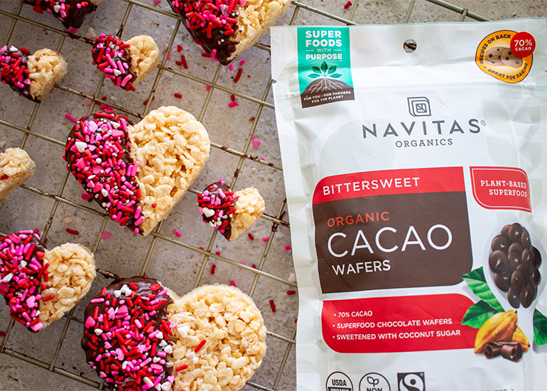 A wire cooling rack topped with chocolate-dipped rice krispy hearts made with Navitas Organics Bittersweet Cacao Wafers, decorated with Valentine's sprinkles