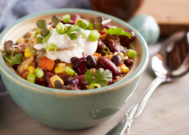 A bowl of chili made with Navitas Organics Chia Seeds, garnished with dairy-free sour cream and chopped green onions