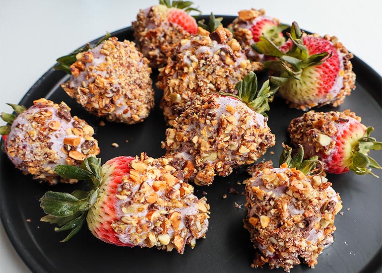 A black plate topped with acai yogurt and granola covered strawberries made with Navitas Organics Acai Powder