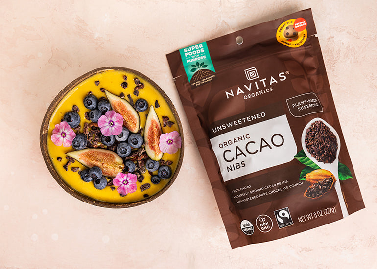 A mango piña colada smoothie bowl topped with Navitas Organics Cacao Nibs, fresh berries and edible flowers