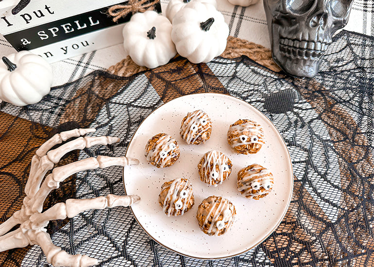 A spooky Halloween scene featuring a plate topped with mummy energy bites made with Navitas Organics Cacao Butter Wafers and Cacao Sweet Nibs