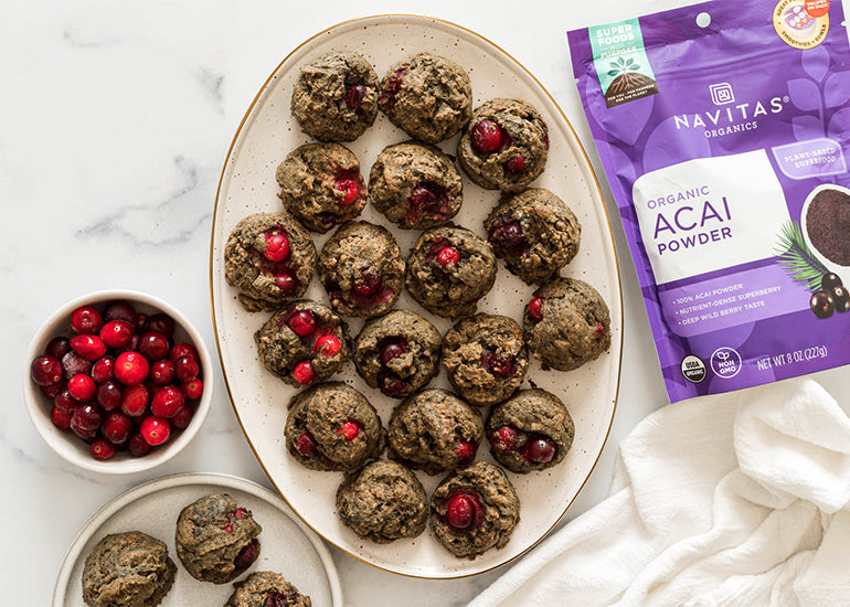 A large plate of cranberry acai cookies next to a bowl of fresh cranberries and a bag of Navitas Organics Acai Powder