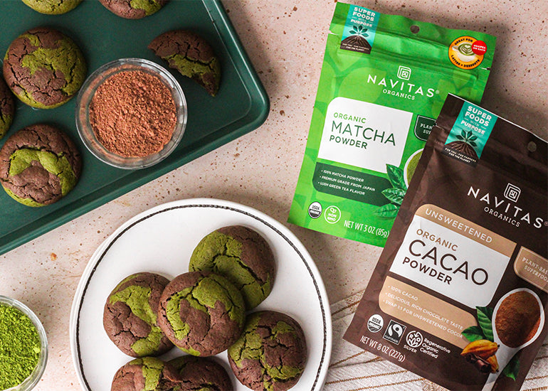 A plate of chocolate matcha marble cookies with dishes and bags filled with Navitas Organics Cacao Powder and Matcha Powder