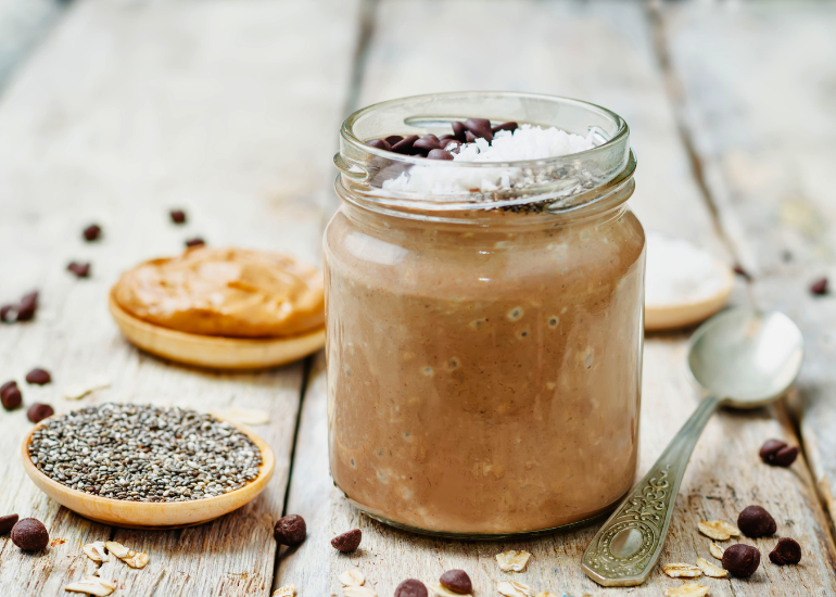 A mason jar filled with chocolate gingerbread overnight oats made with Navitas Organics Chia Seeds and Cacao Powder, next to dished filled with chia seeds and nut butter, and a spoon