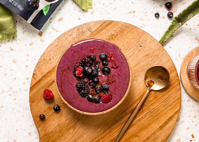 A bowl of homemade maqui berry ice cream topped with assorted berries, served on a wooden platter with a golden spoon.