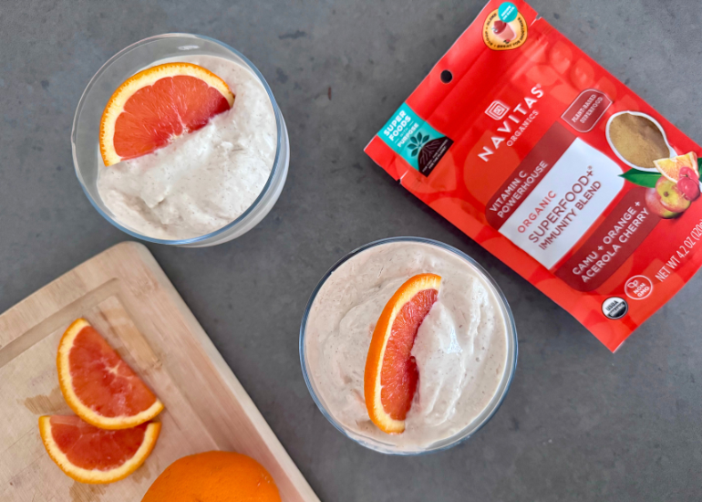 Two glass dishes filled with a homemade ice cream, topped with orange slices, alongside fresh orange slices and a bag of Navitas Organics Superfood+ Immunity Blend on a kitchen counter.