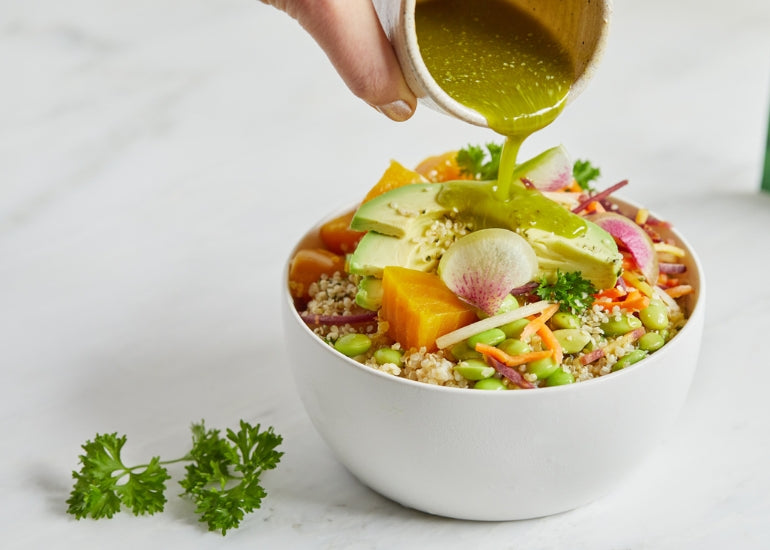 A bowl full of grains and fresh vegetables being drizzled with a vinaigrette made with Navitas Organics Wheatgrass Powder.