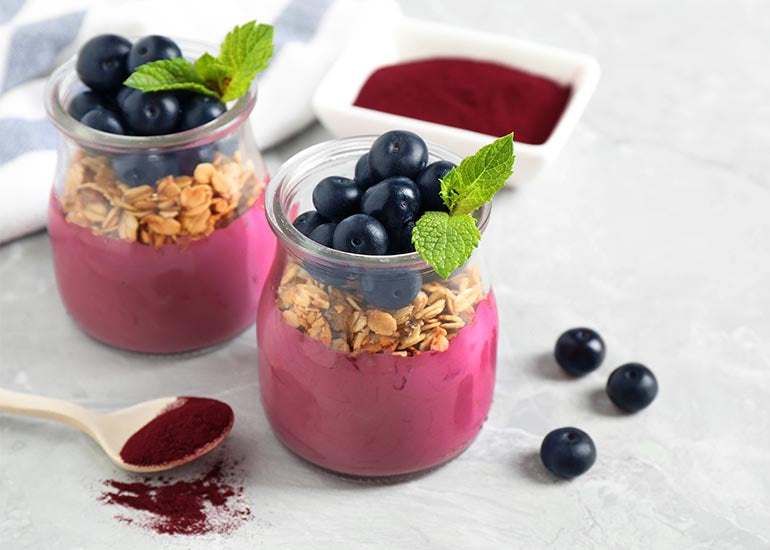 Two glass jars filled with a yogurt parfait mixed with immune-boosting superfoods, surrounded by fresh blueberries