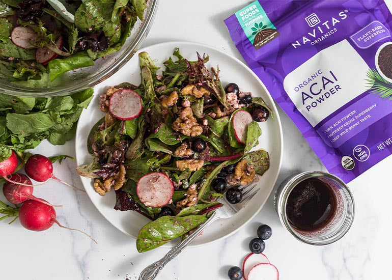 A plate filled with a green salad and a glass dish with a vinaigrette made with Navitas Organics Acai Powder