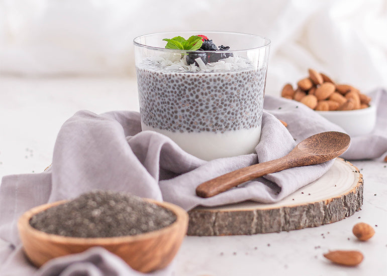 A glass dish filled with chia pudding aside a wooden bowl filled with Navitas Organics Chia Seeds.