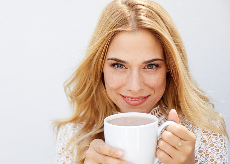 A woman holding a mug of hot cocoa made with Navitas Organics Cacao Powder.