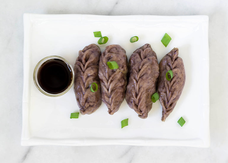 A plate of homemade maqui berry dumplings garnished with green onions beside a small glass dish filled with dipping sauce.