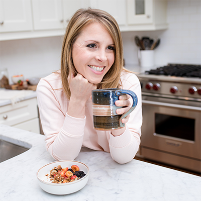 Integrative Nutritionist and Women's Wellness Expert Erin Parekh at her kitchen counter drinking coffee and eating a yogurt bowl topped with Navitas Organics superfoods
