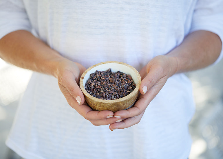 A woman holding a wooden bowl filled with Navitas Organics Cacao Nibs.