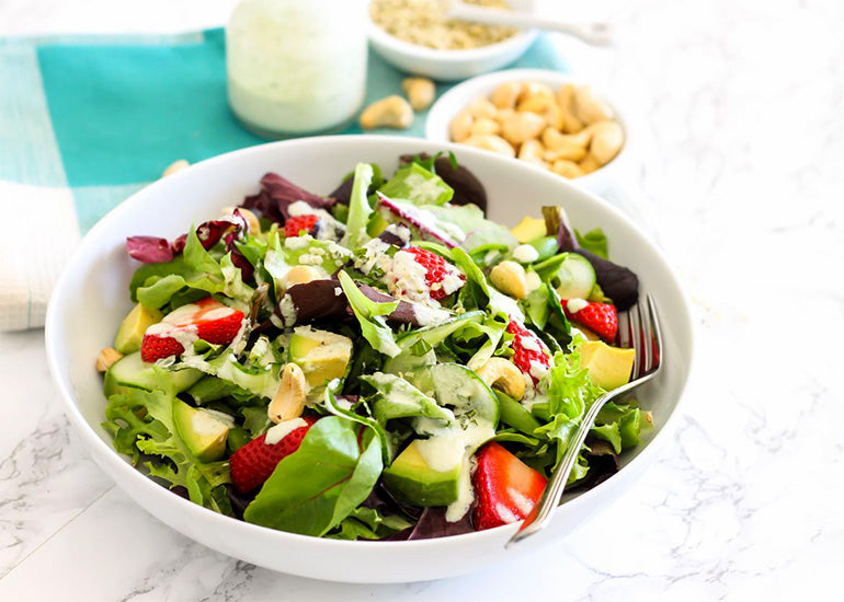 A summery spinach and strawberry salad in a bowl, topped with Navitas Organics Cashew Nuts and Hemp Seeds