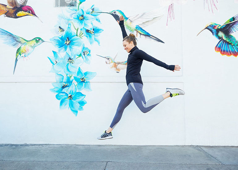 A woman in workout gear jumping for joy on a sidewalk.