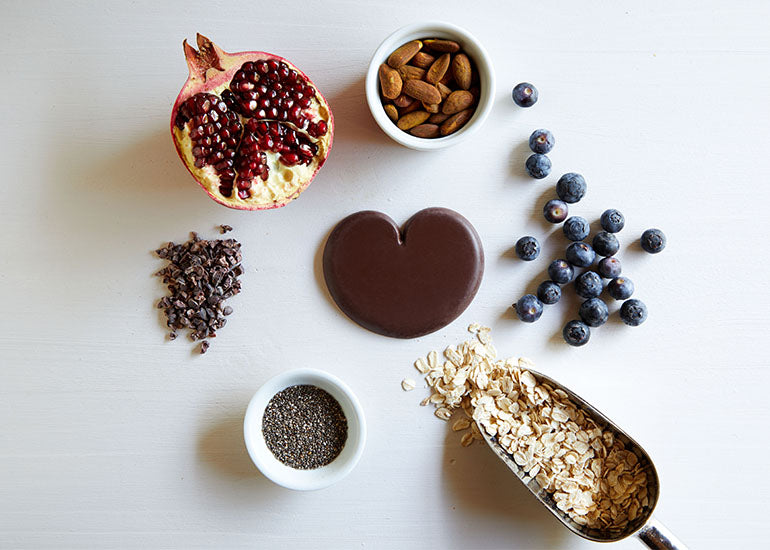 A pomegranate, blueberries, oats, almonds, and Navitas Organics Cacao Nibs spread out on a countertop