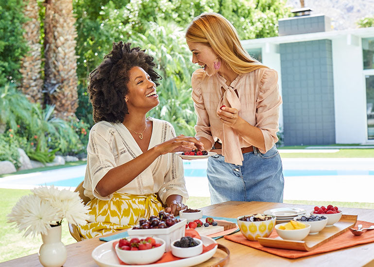 A woman serving a plate of fresh food to another woman at a table.