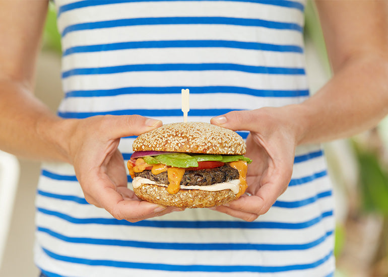 A woman holding a veggie burger prepared with Navitas Organics superfood ingredients.