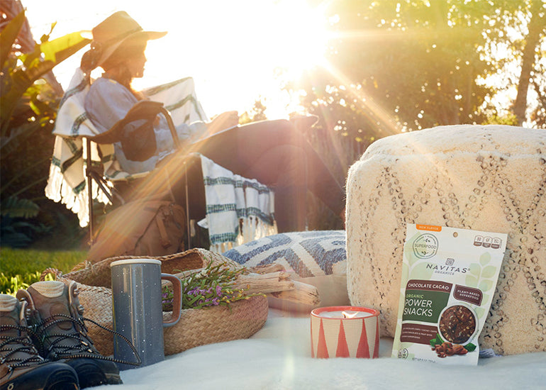A woman sitting in a chair under the sun with Navitas Organics Power Snacks in the foreground.