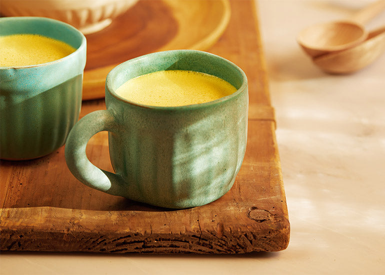Two mugs filled with golden milk lattes made with Navitas Organics Turmeric Powder