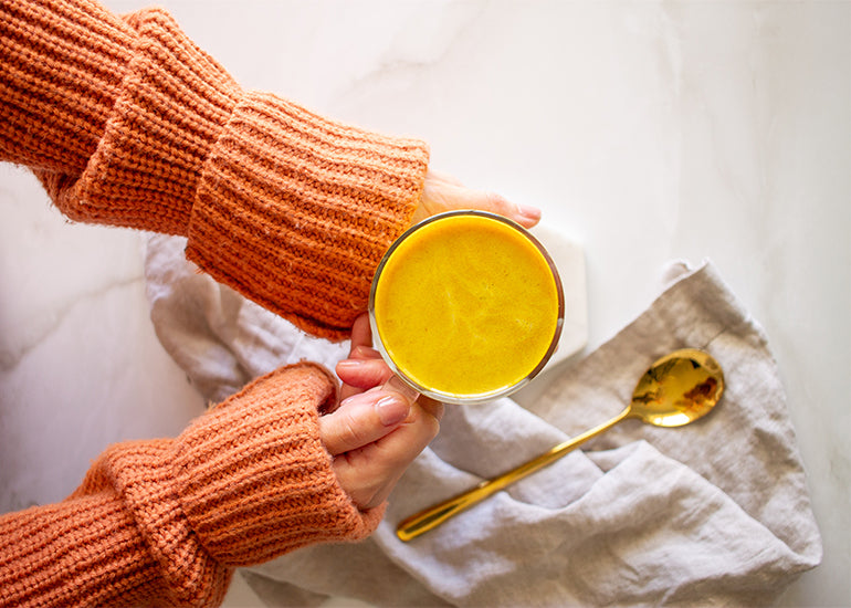 A woman in an orange sweater holding a golden turmeric latte in a mug, made with Navitas Organics Golden Turmeric Latte Mix