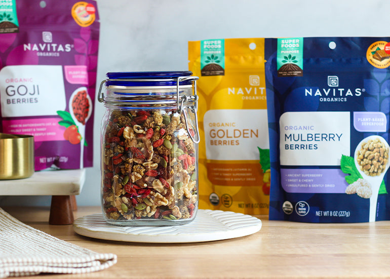 A mason jar filled with trail mix on a wooden surface surrounded by bags of Navitas Organics Goji Berries, Goldenberries and Mulberries