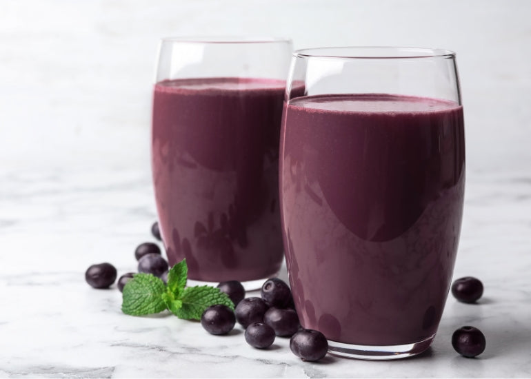 Two acai smoothies in tall glasses surrounded by acai berries