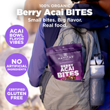 Advertisement for Navitas Organics Berry Acai Bites, emphasizing the product as small bites with big flavor and real, organic ingredients. The image shows a close-up of a person holding a bag of the berry bites while hiking, with scenic mountainous backdrop. Text includes health claims like 'No artificial ingredients' and 'Certified gluten-free.'