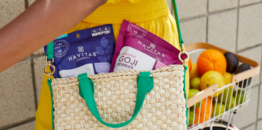 A woman carrying two Navitas Organics with her shopping cart