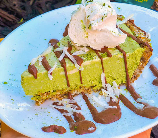 Slice of green Navitas Organics Matcha Powder cheesecake topped with coconut whipped cream and drizzled with caramel sauce