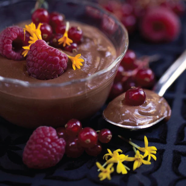Glass bowl of whipped chocolate mousse decorated with strawberries and edible flowers