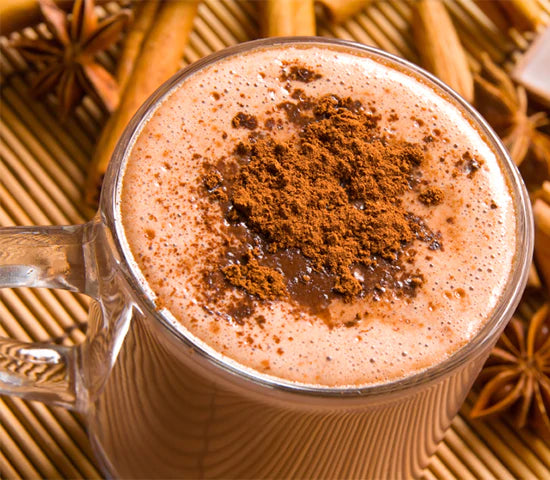 Glass mug of hot cocoa sprinkled with Navitas Organics Cacao Nibs and Cacao Powder