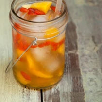 Glass ball jar with an iced sake sangria recipe steeped with goji berries and mango chunks