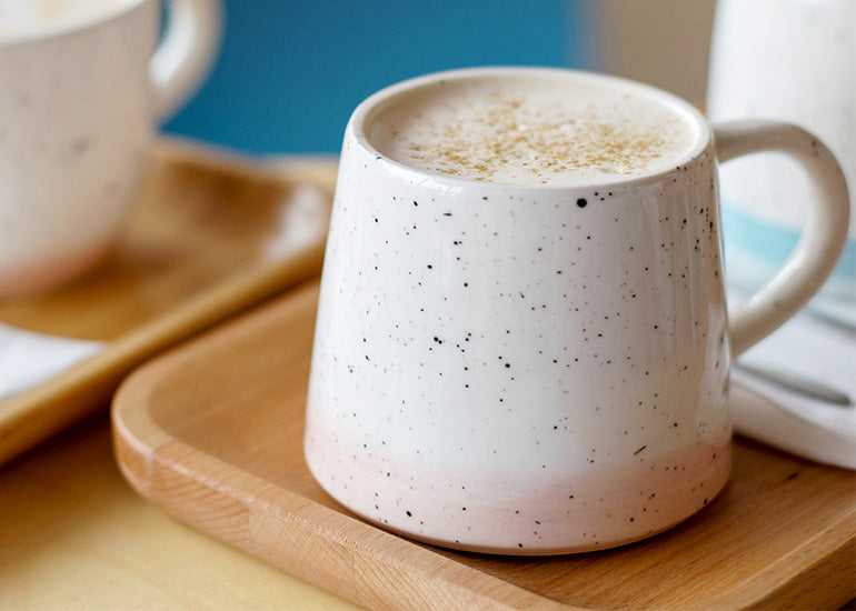 A latte made with Navitas Organics Cacao Butter and coffee in a ceramic mug on a wooden serving tray
