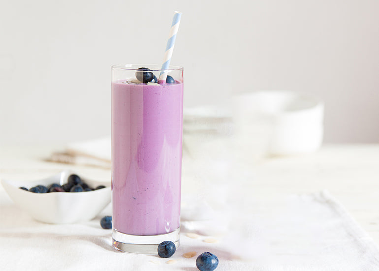 A smoothie made with Navitas Organics Pomegranate Powder in a tall glass, topped with fresh blueberries