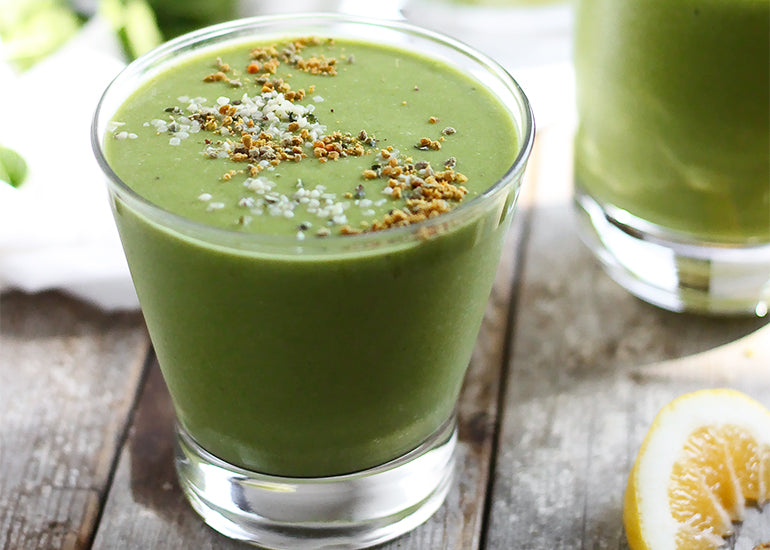 A green smoothie in a glass made with fruit and Navitas Organics Hemp Seeds, topped with bee pollen and Navitas Organics Hemp Seeds and Chia Seeds 