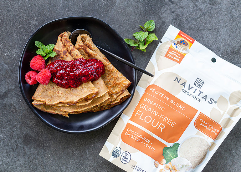Crepes made with Navitas Organics Grain-Free Flour folded on a plate, topped with jam, fresh raspberries and mint
