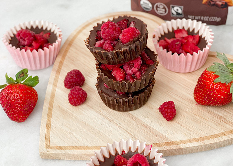 Dark chocolate cups made with Navitas Organics Cacao Powder and Cacao Butter, topped with fresh raspberries on a heart-shaped wooden cutting board
