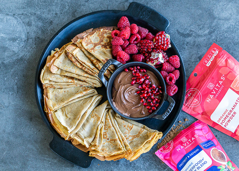 A plate full of crepes made with Navitas Organics Superfood+ Berry Blend and Pomegranate Powder, along with a dish full of chocolate dip and a side of fresh berries