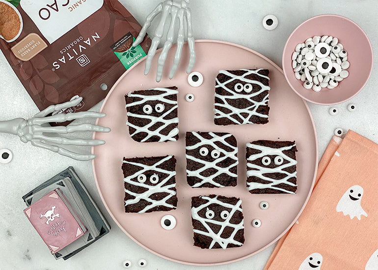 A plate full of chocolate brownies made with Navitas Organics Cacao Powder, decorated as mummies with white icing and candy eyes