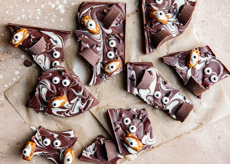 Chocolate bark made with Navitas Organics Cacao Butter Wafers, Cacao Powder and Cacao Nibs, decorated with pretzels, candy eyes and chocolate peanut butter cups