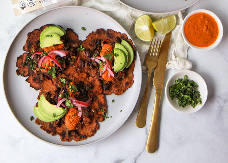 A plate of tostadas made with Navitas Organics Cauliflower Flour, topped with black beans, avocado, red onion and cilantro