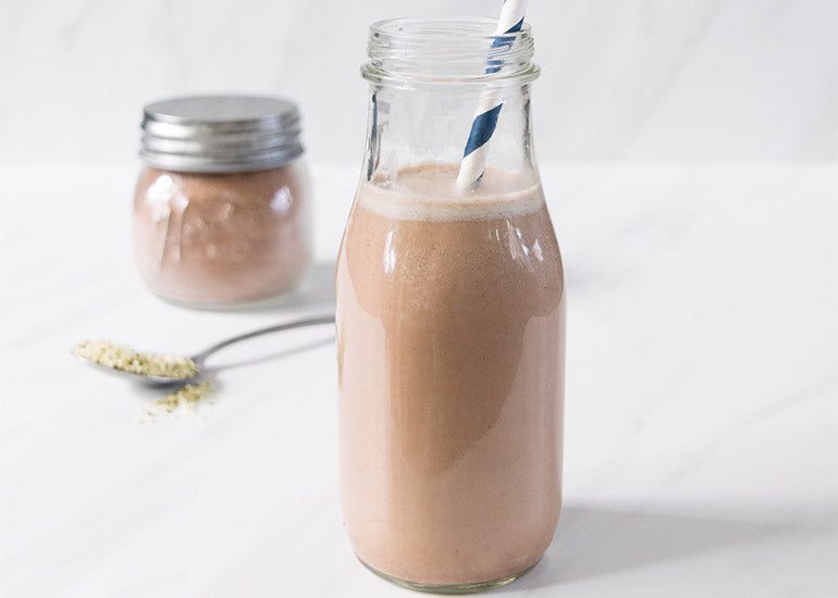 A tall glass filled with chocolate milk made with Navitas Organics Hemp Seeds and Cacao+ Longevity Blend