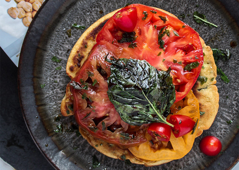 A stack of savory pancakes made with Navitas Organics Chickpea Flour, topped with slices of tomato and fresh basil