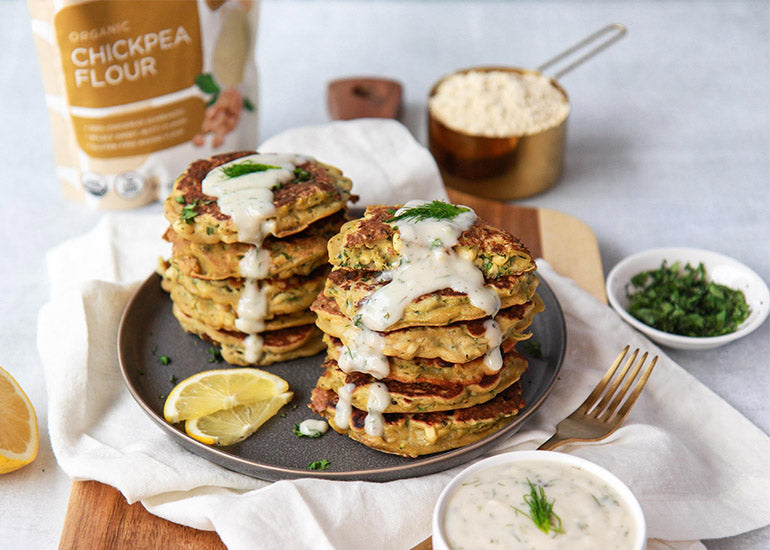 Two stacks of corn and zucchini fritters made with Navitas Organics Chickpea Flour, topped with dill garlic yogurt sauce