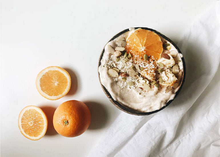 A smoothie bowl made with Navitas Organics Vanilla & Greens Essential Blend and Superfood+ Immunity Blend topped with fresh orange slices, almonds, coconut, and Navitas Organics Hemp Seeds